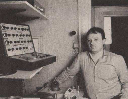 Musician seated beside a home-built electronic console in a small studio